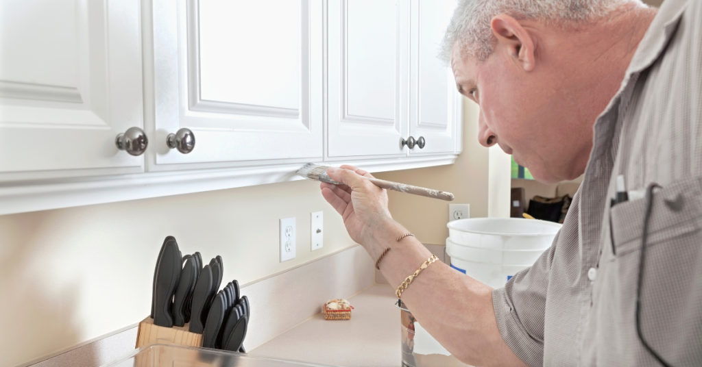 An image of a professional painter from Cabinet Refinishing North Bay applying a fresh coat of paint to cabinets with wood surfaces.